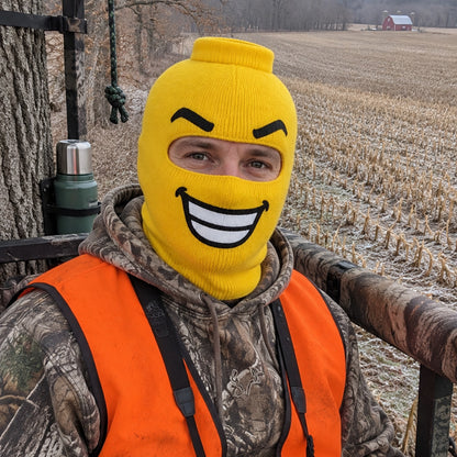 Hunter in a tree stand wearing the BUCK GRIN balaclava over a frosted cornfield